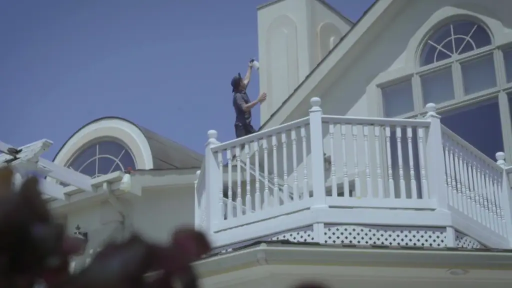 A tech on a second-storey white balcony cleaning an arched window