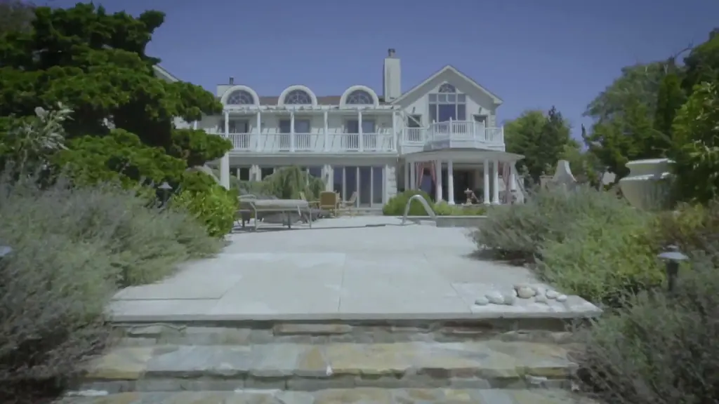 Bluestone steps and a pale stone terrace leading up to a shingled house with arched dormers and lavender borders