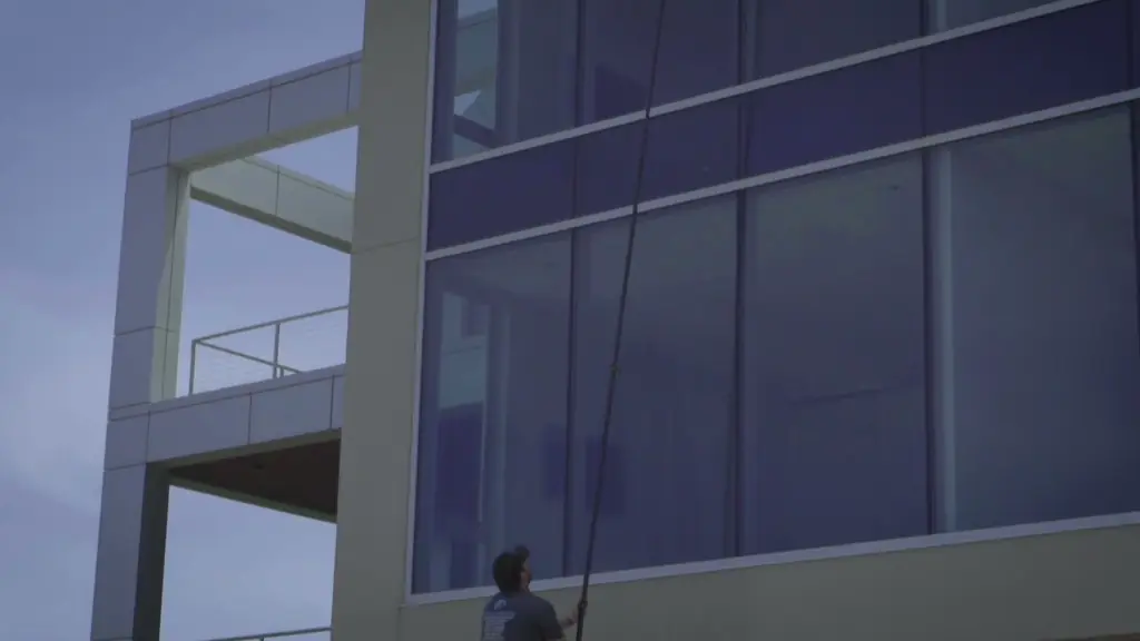 A Clean Hamptons tech running a water-fed pole up the two-storey glass wall of a modern white house