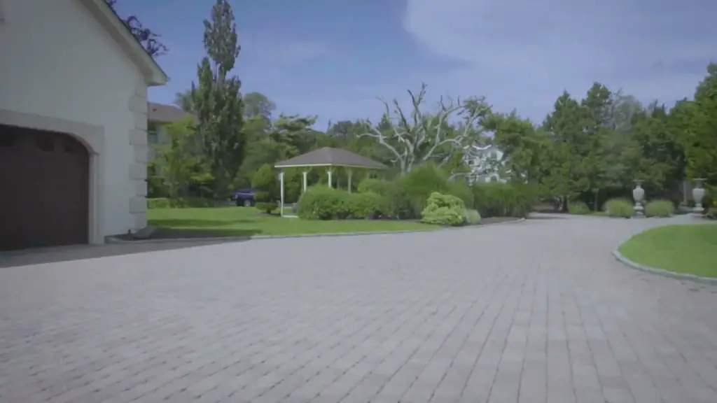 A wide brick-paver motor court beside a garage, a gazebo and clipped lawn beyond