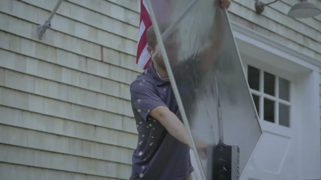 A Clean Hamptons tech carrying a washed window screen past cedar shingle siding and a white carriage door