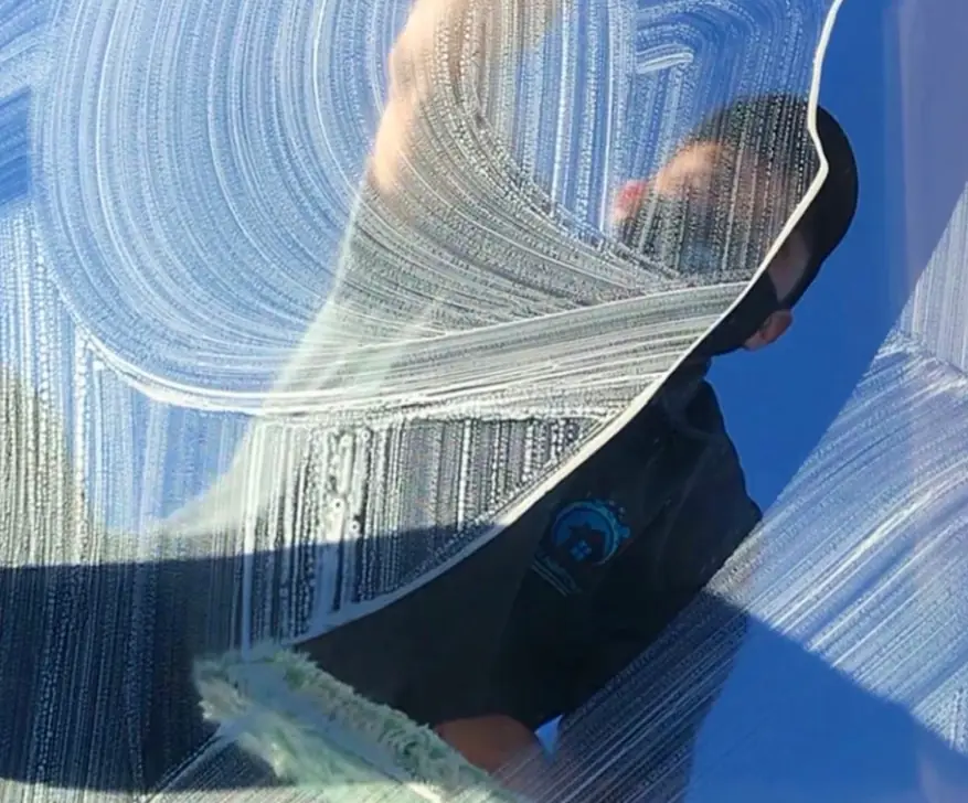 A crew member's reflection behind a squeegee wipe across a pane of glass