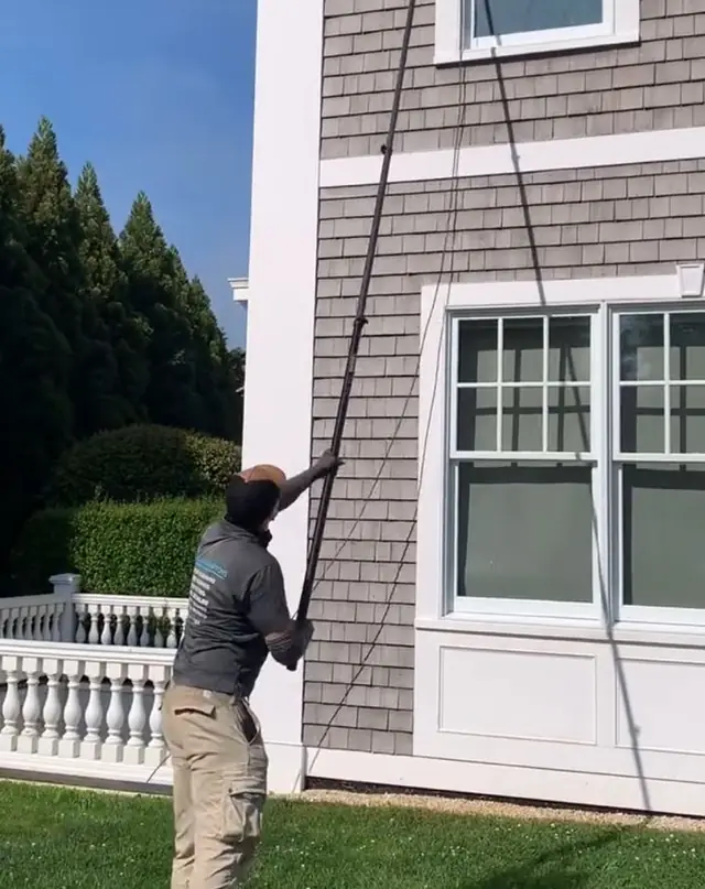 A Clean Hamptons tech on the lawn working a water-fed pole up a grey-shingled house