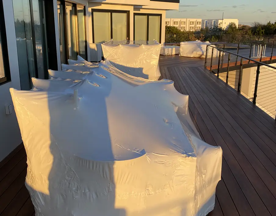 Outdoor furniture shrink wrapped in white on a wooden deck at golden hour