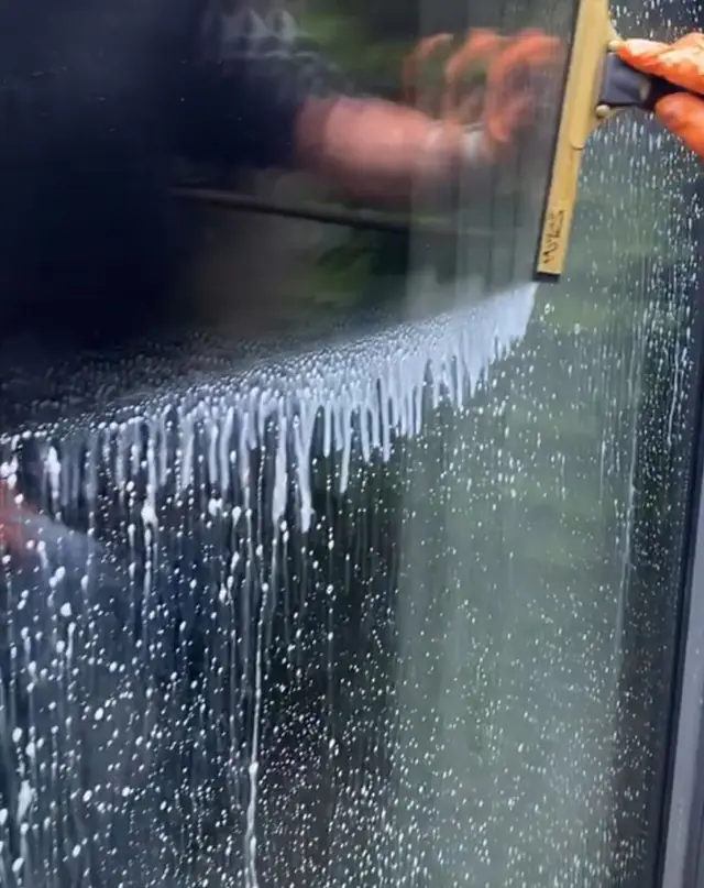 A squeegee pulling a level line of water down a pane of glass